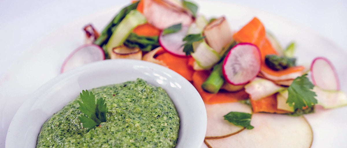 Creamy green Thai pesto beside colorful vegetable pasta with asparagus, carrot ribbons, radishes, and fresh herbs.