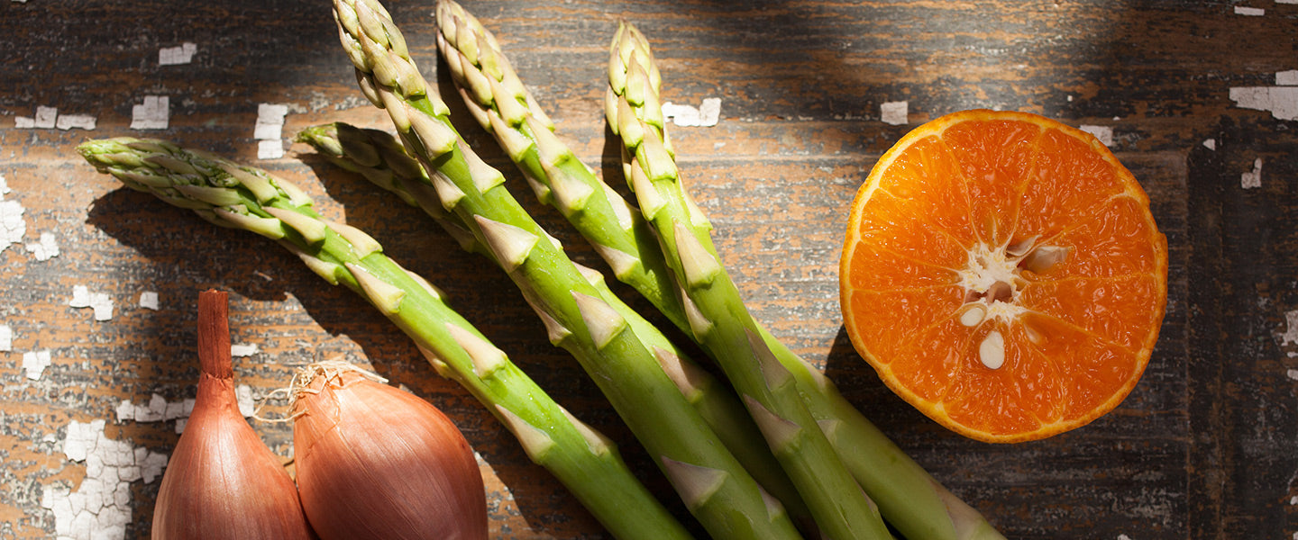 Fresh asparagus spears, two shallots, and a halved orange.