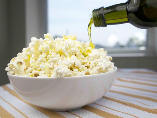 Extra virgin olive oil being drizzled from a bottle over freshly popped popcorn.