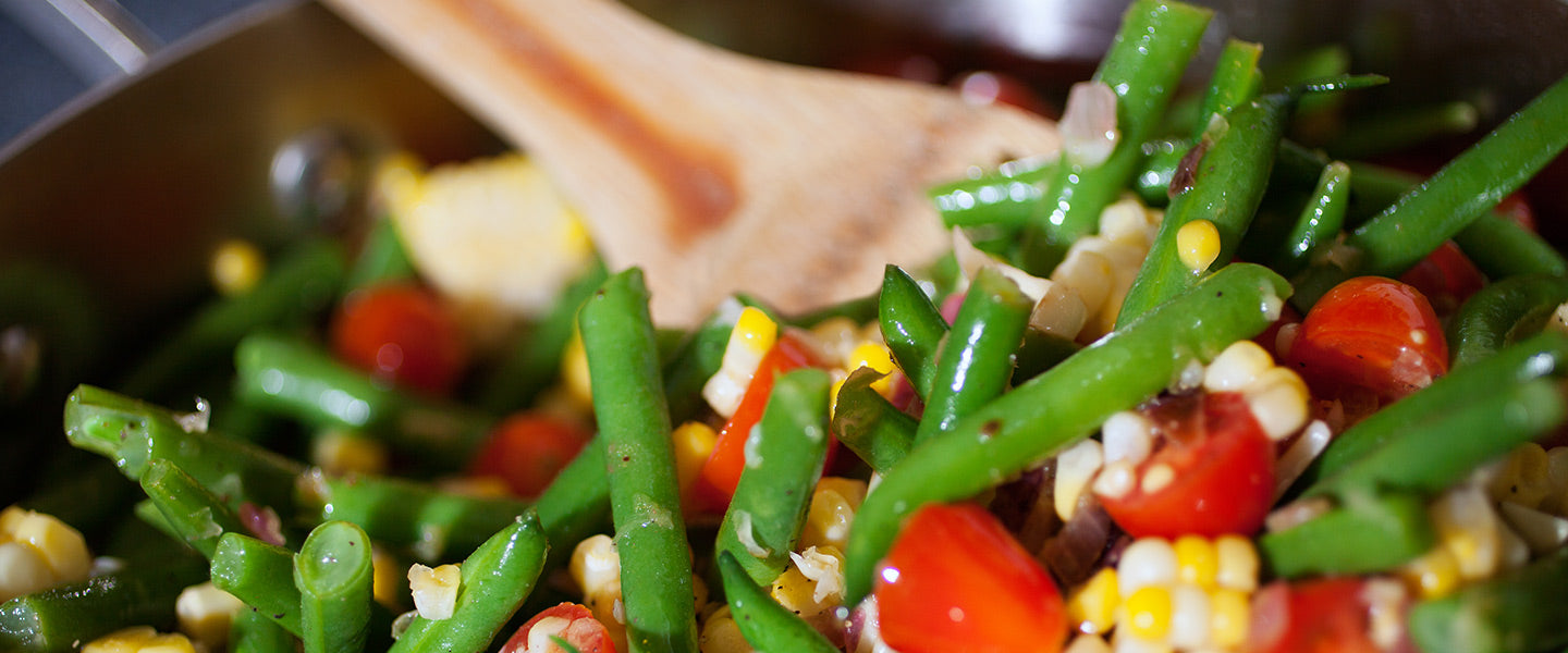 Green bean salad with sweet corn, cherry tomatoes, and red onion being tossed.
