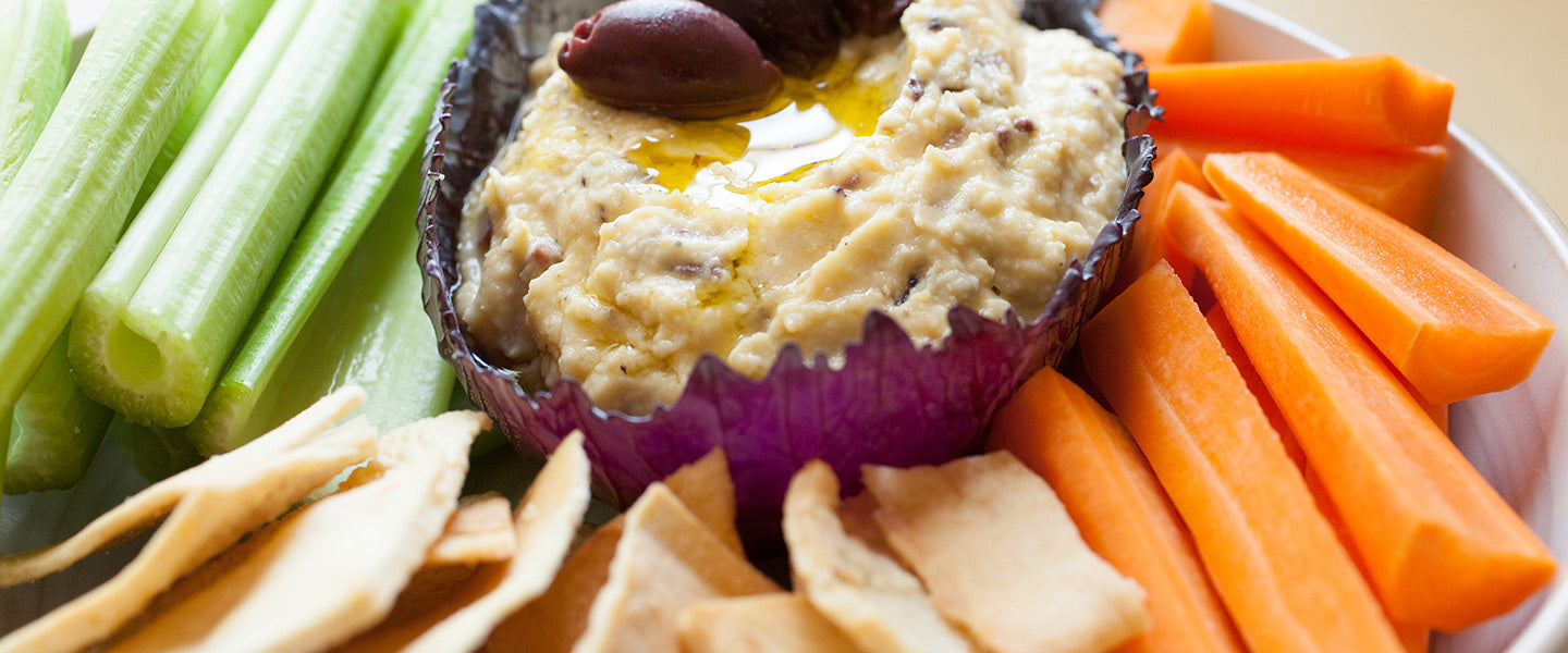 Creamy hummus drizzled with olive oil and topped with olives, served with celery, carrot sticks, and pita chips.