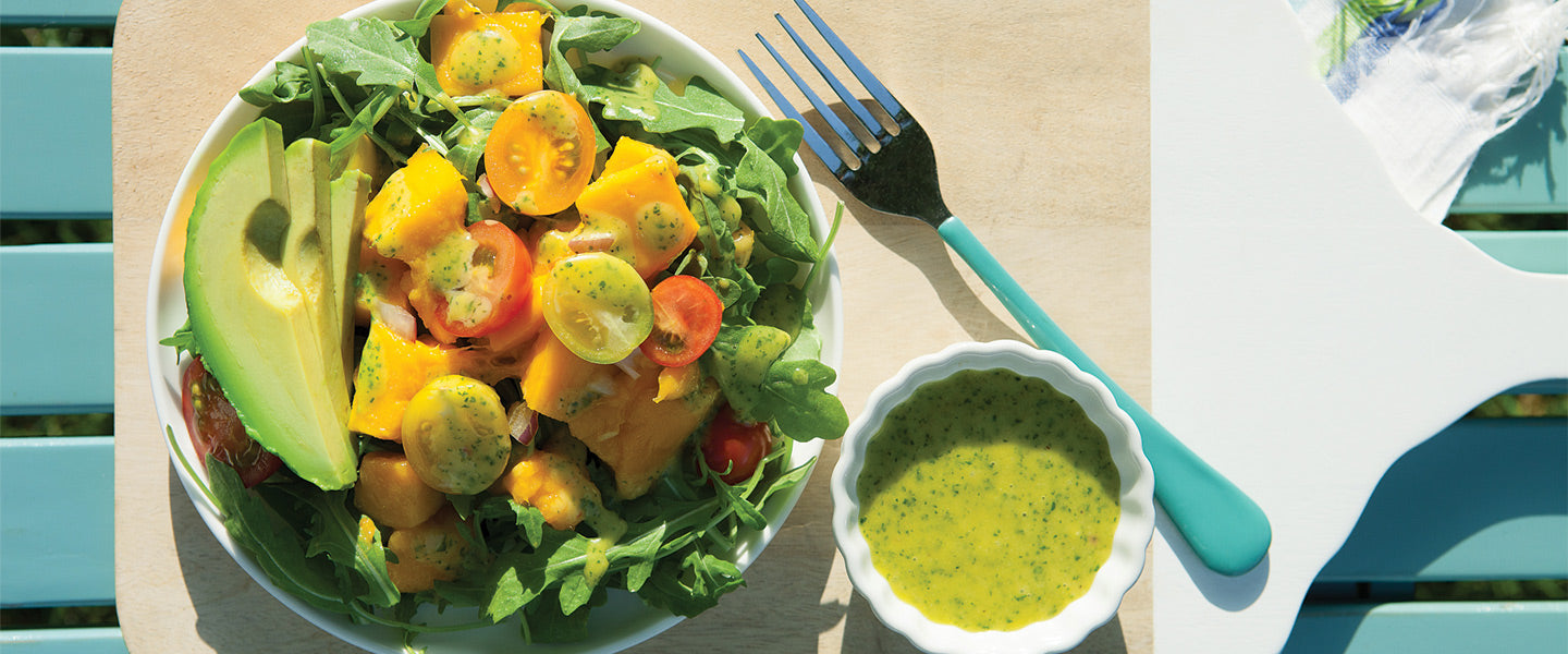 Mango avocado salad with arugula, cherry tomatoes, and herb dressing served in bright sunlight.