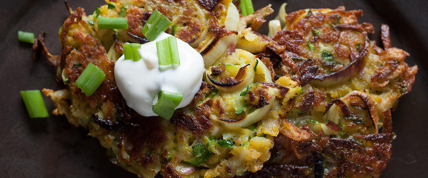 Crispy potato and zucchini latkes topped with sour cream and chopped green onions.