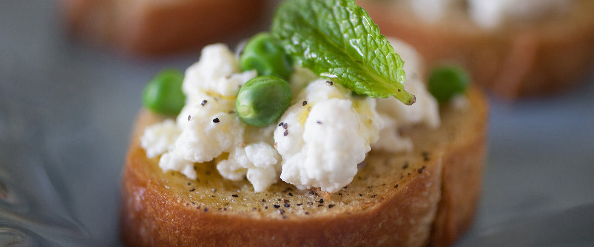 Toasted crostini topped with creamy ricotta, green peas, fresh mint, black pepper, and olive oil.