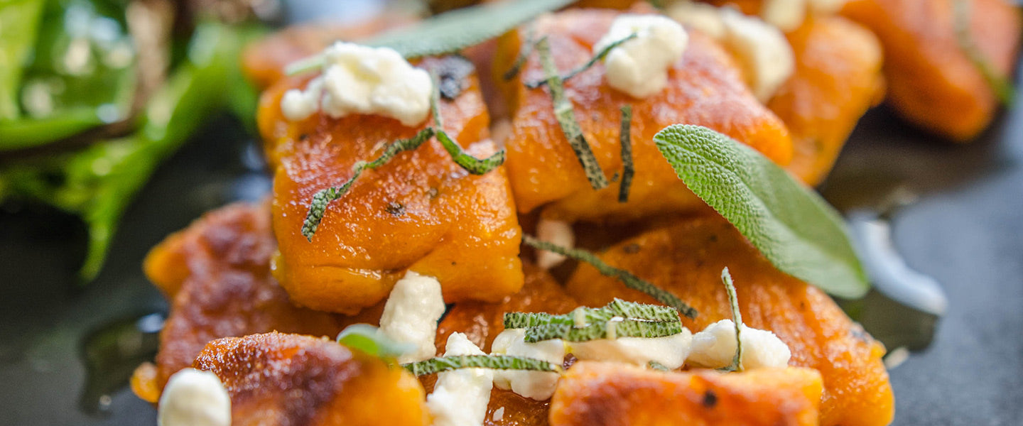 Sweet potato gnocchi topped with creamy goat cheese and fresh sage, served alongside a green salad.