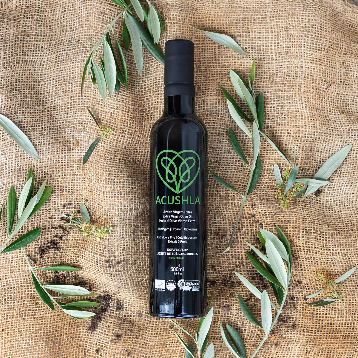 A 500 ml bottle of Acushla Organic DOP Trás-os-Montes surrounded by olive branches.