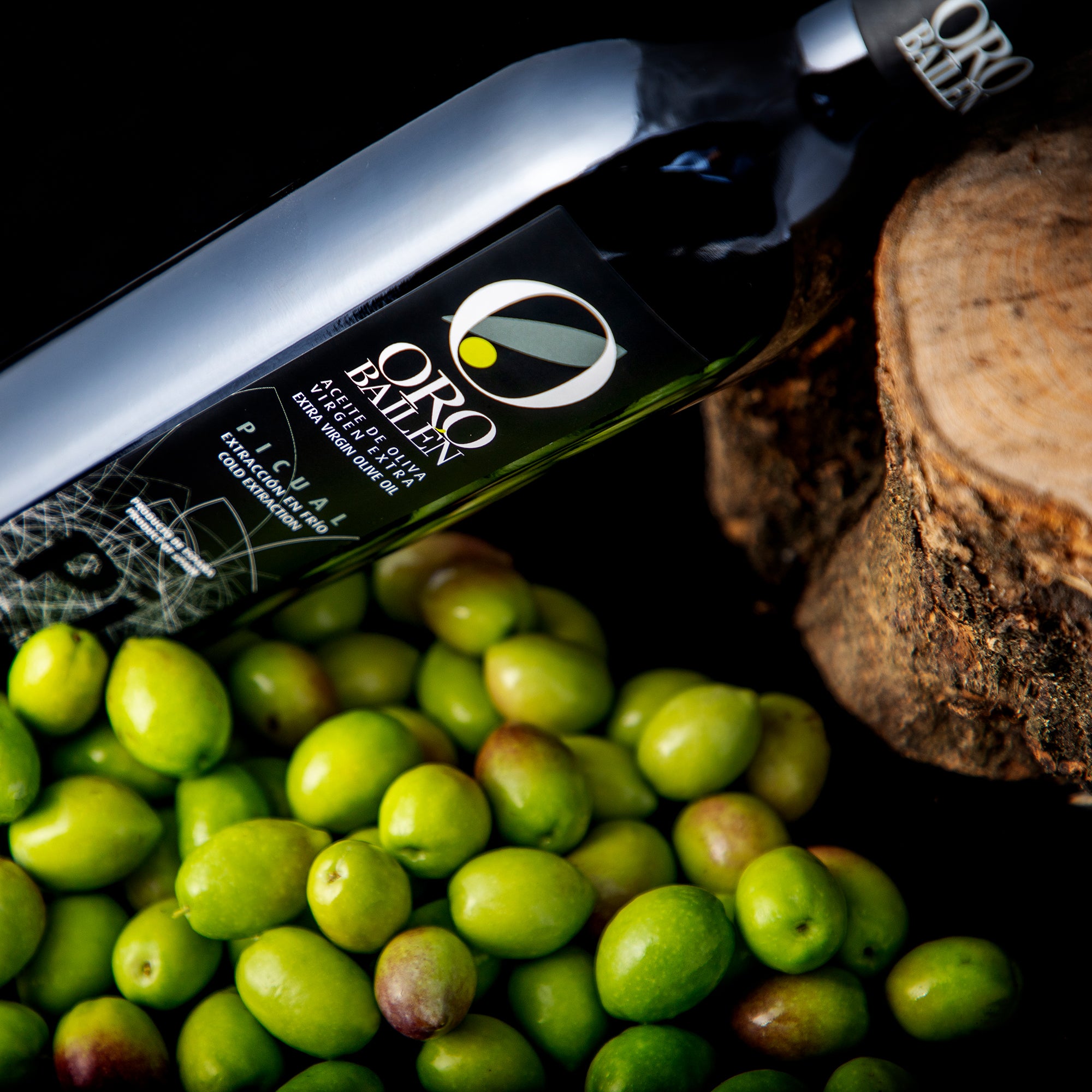 Oro Bailen Reserva Familiar Picual 500ml bottle beside fresh olives and a rustic wooden log.