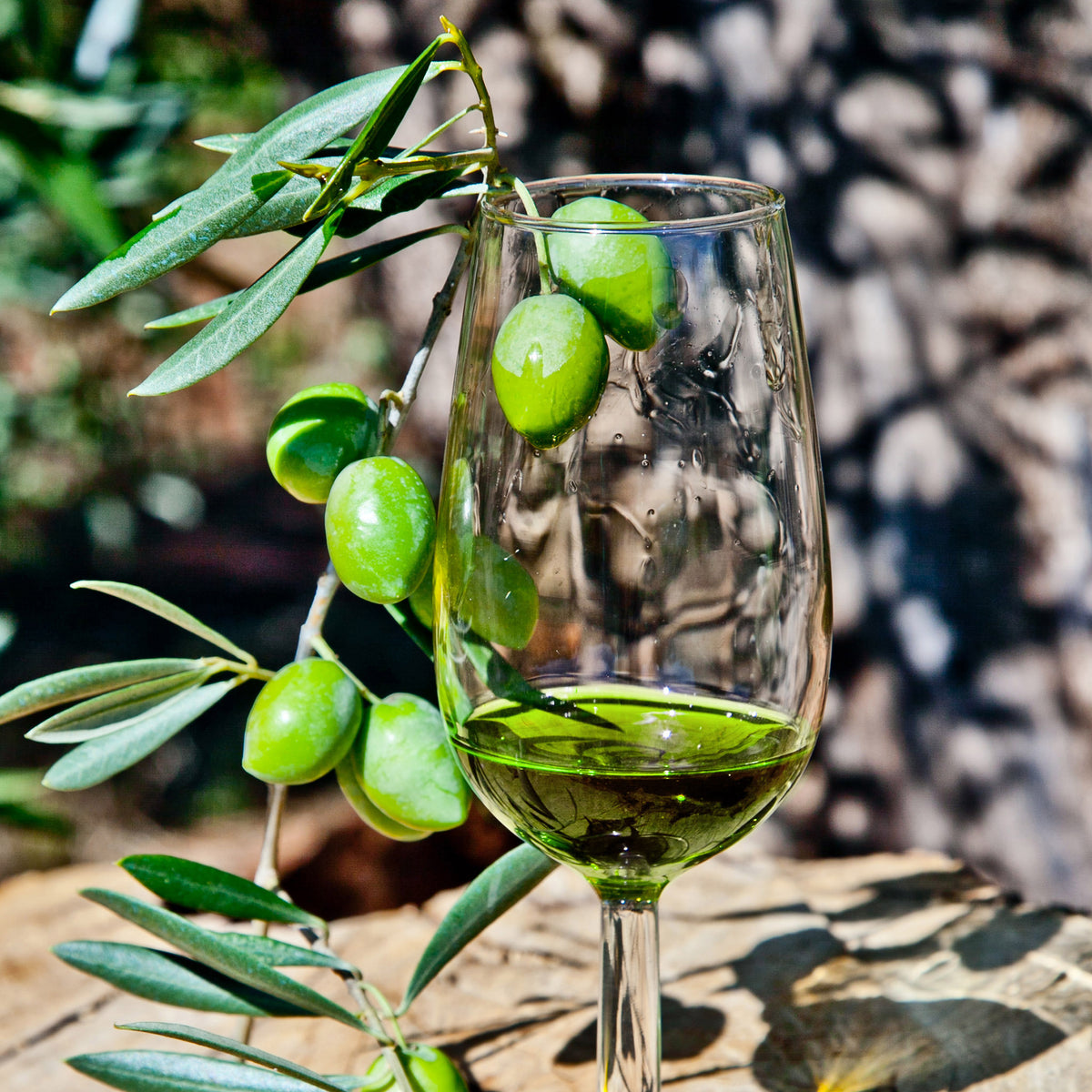Green Picual olives beside a glass filled with vivid green olive oil.