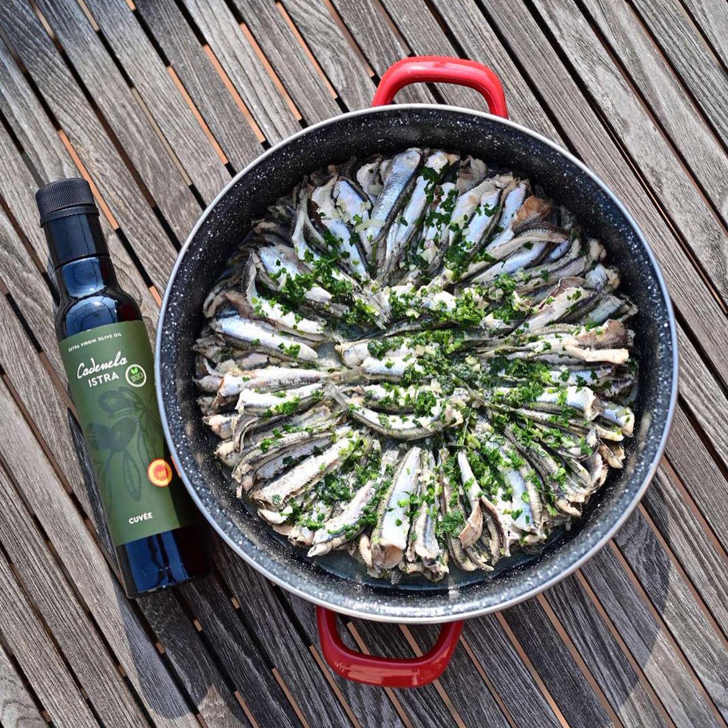 Cadenela Cuvée St. Lucia DOP Istra Organic olive oil bottle beside a pan of herb-topped fish.