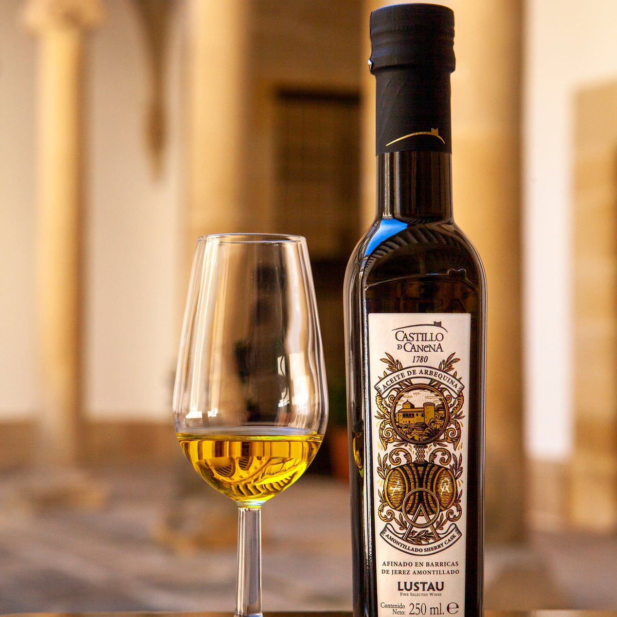 250 ml bottle of Castillo de Canena Arbequina Amontillado Sherry Cask beside a glass of olive oil.