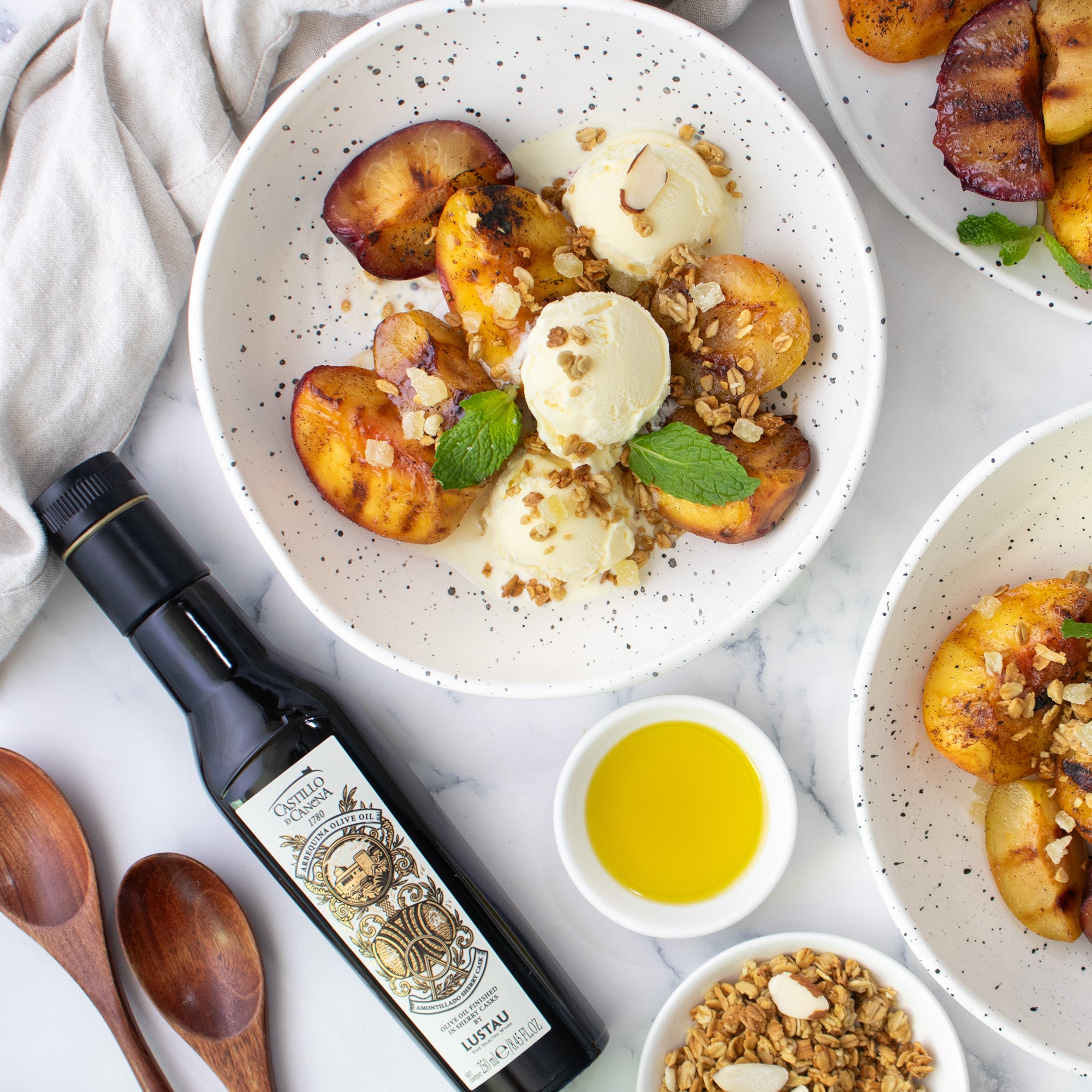 Castillo de Canena Arbequina Amontillado Sherry Cask olive oil beside grilled peaches, ice cream, granola, and mint.