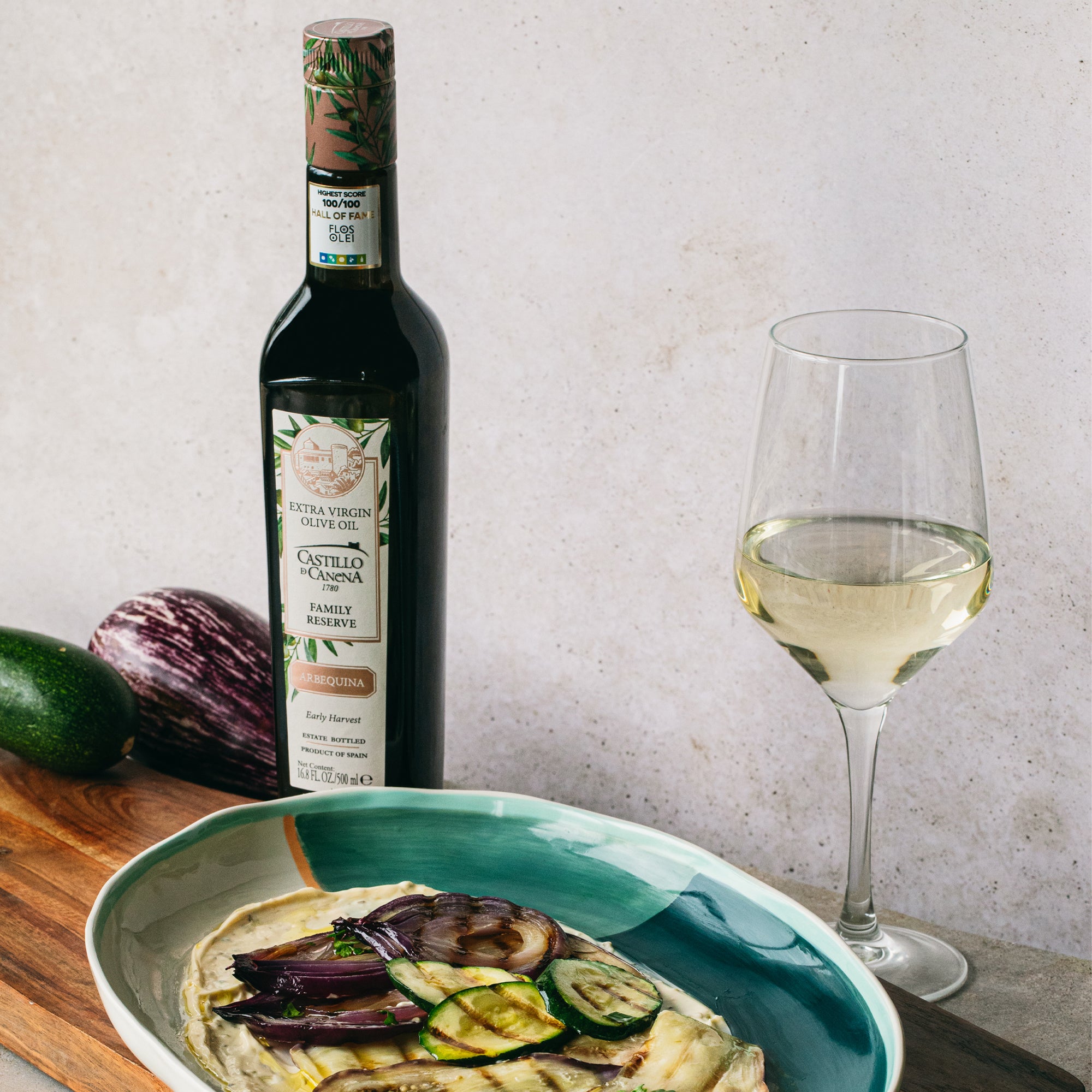 500 ml bottle of Castillo de Canena Family Reserve Arbequina beside grilled vegetables and a glass of white wine.