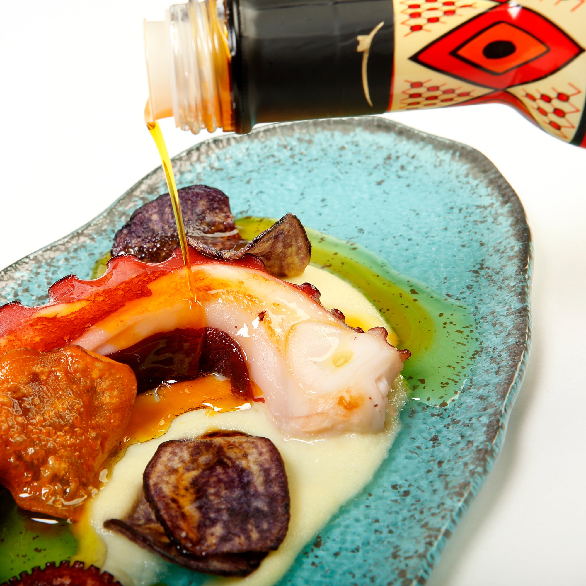 Castillo de Canena Harissa Arbequina olive oil being poured over octopus, potatoes, and sauce.