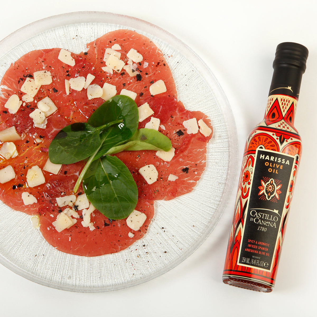 Castillo de Canena Harissa Arbequina bottle beside sliced beef topped with cheese, spinach, and seasoning.