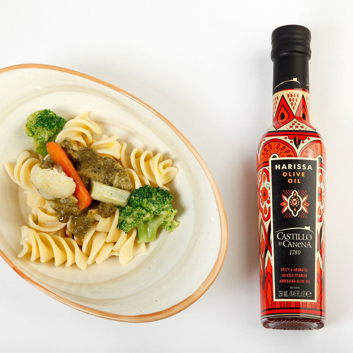 Castillo de Canena Harissa Arbequina 250 ml bottle beside pasta with broccoli, cauliflower, and carrots.