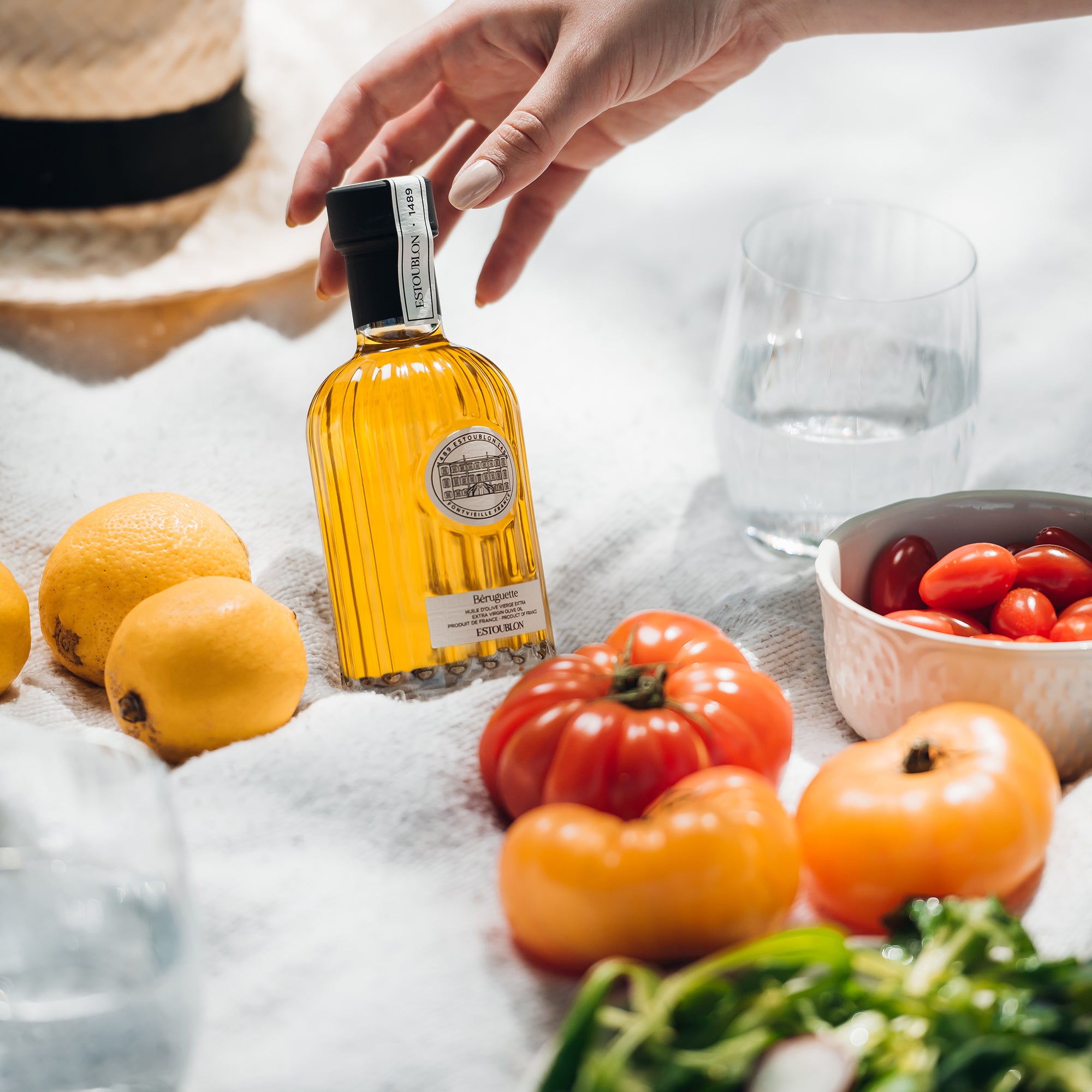Estoublon Beruguette olive oil bottle surrounded by fresh tomatoes, lemons and vegetables.