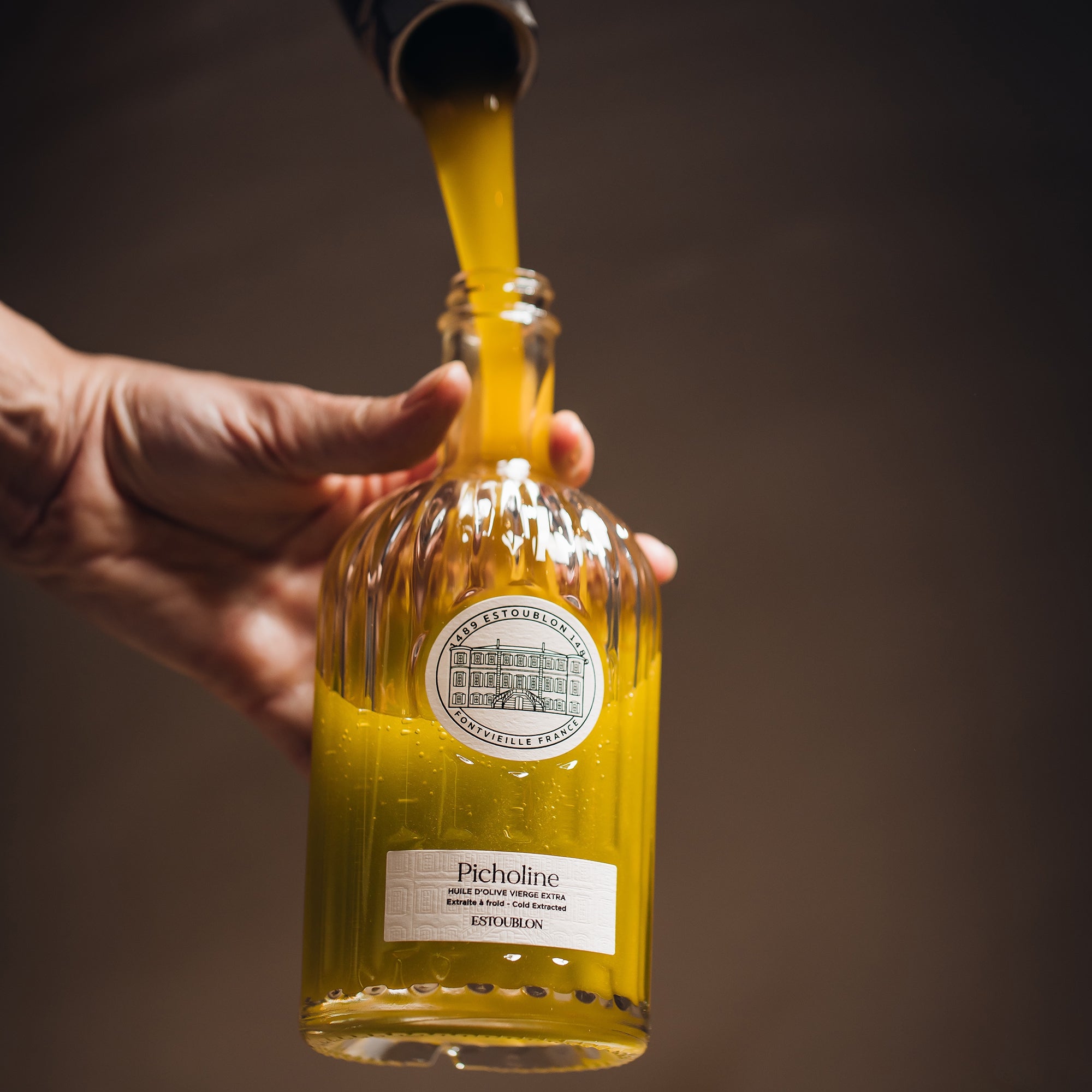 Olive oil pours into a hand-held Estoublon Picholine bottle during production.