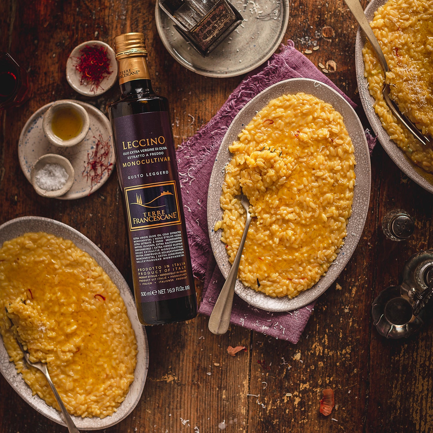 500 ml bottle of Terre Francescane Leccino olive oil surrounded by plates of creamy saffron risotto.