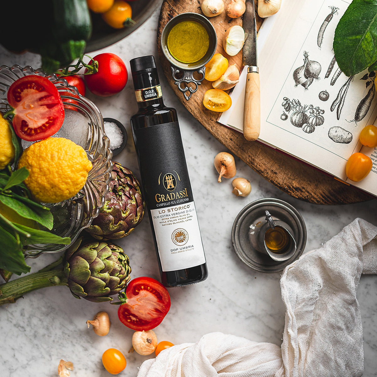 Gradassi Lo Storico extra virgin olive oil bottle beside artichokes, tomatoes, and onions.