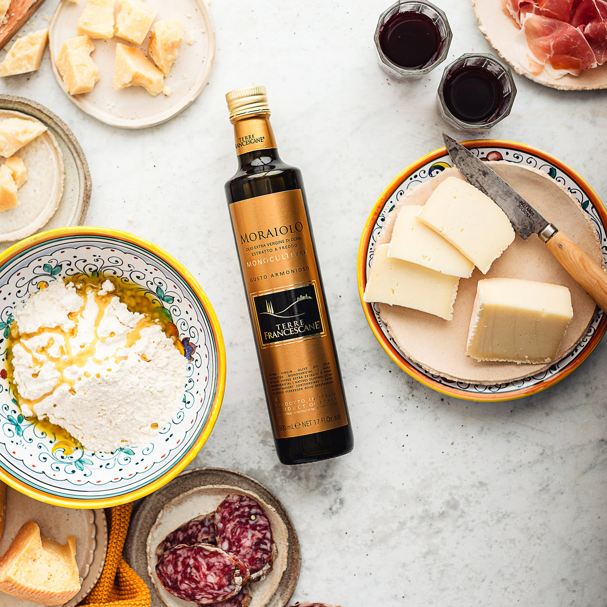 500 ml Terre Francescane Moraiolo bottle surrounded by cheeses, cured meats, ricotta, and glasses of red wine.
