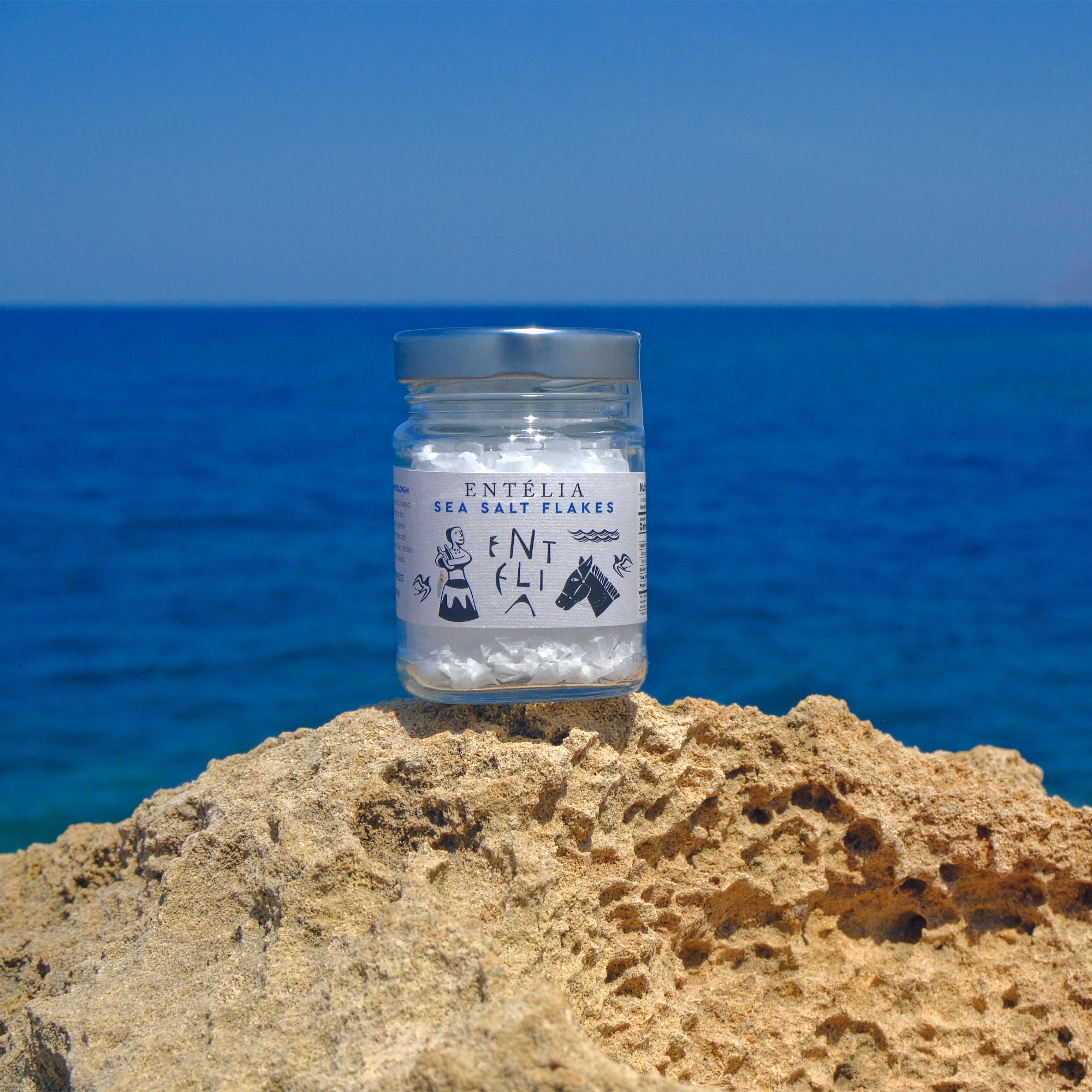 100g jar of Entelia Pyramid Sea Salt Flakes on coastal rocks in Crete, Greece.