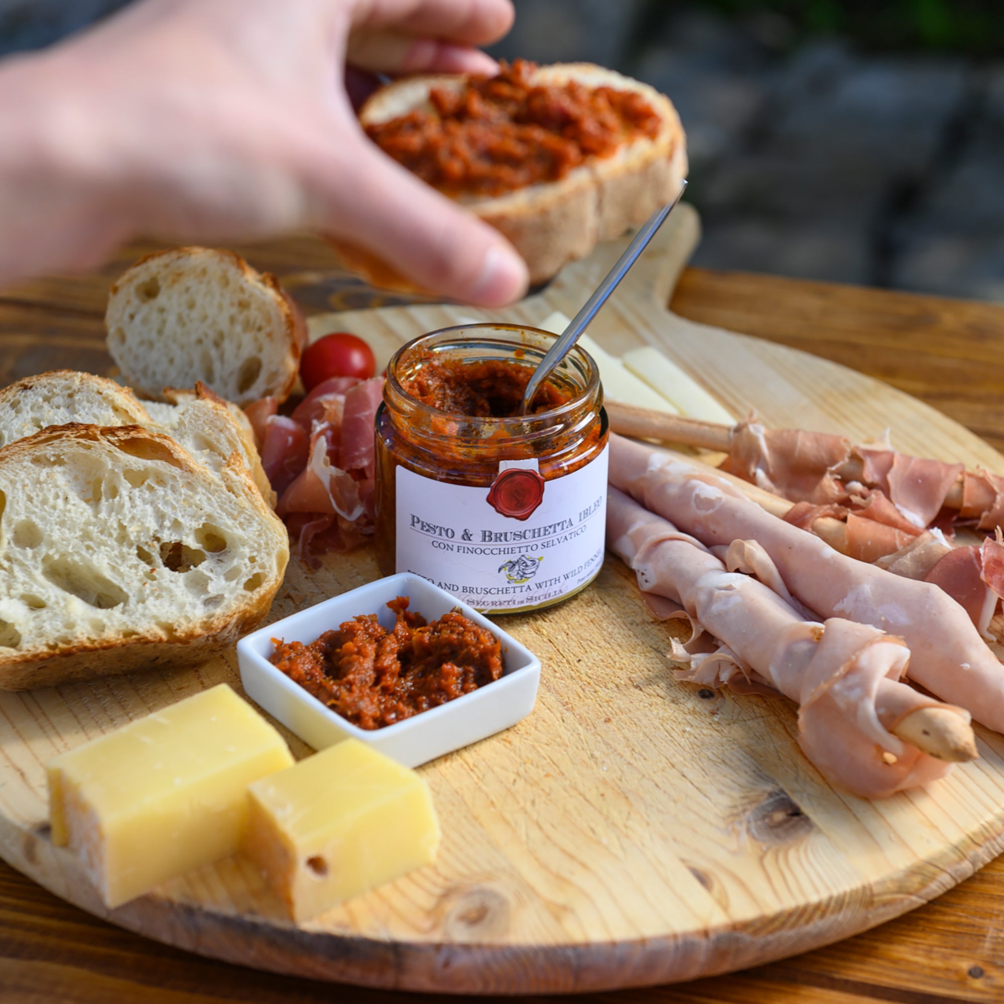 Slice of bread spread with Frantoi Cutrera Pesto and Bruschetta, served with cheese, cured meats, and tomatoes.