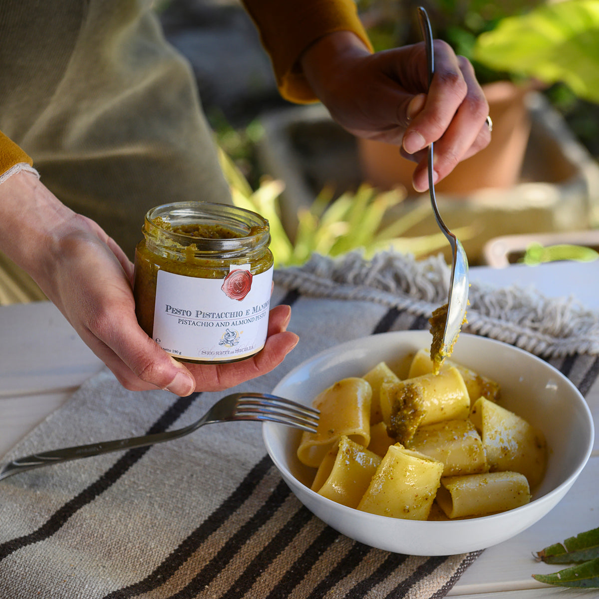 Adding Frantoi Cutrera Pistachio and Almond Pesto from a 190g jar to a bowl of paccheri.