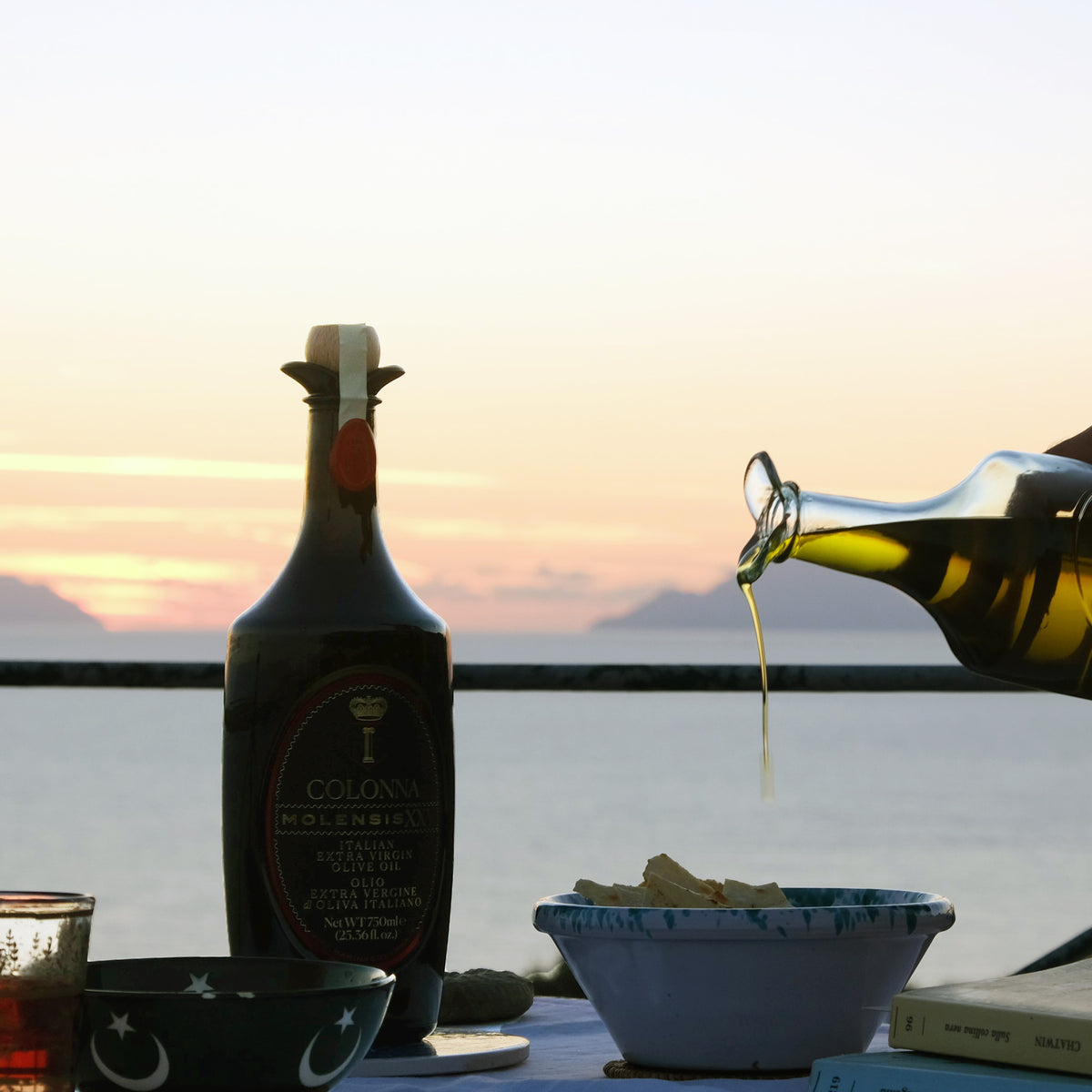Colonna Molensis XXV 750 ml bottle at sunset beside bowls as olive oil pours.