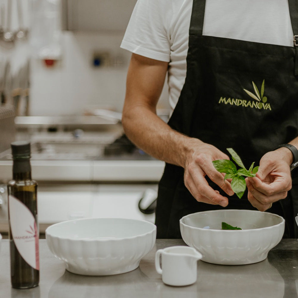 A bottle of Mandranova Cerasuola beside a chef adding fresh basil leaves to a bowl.