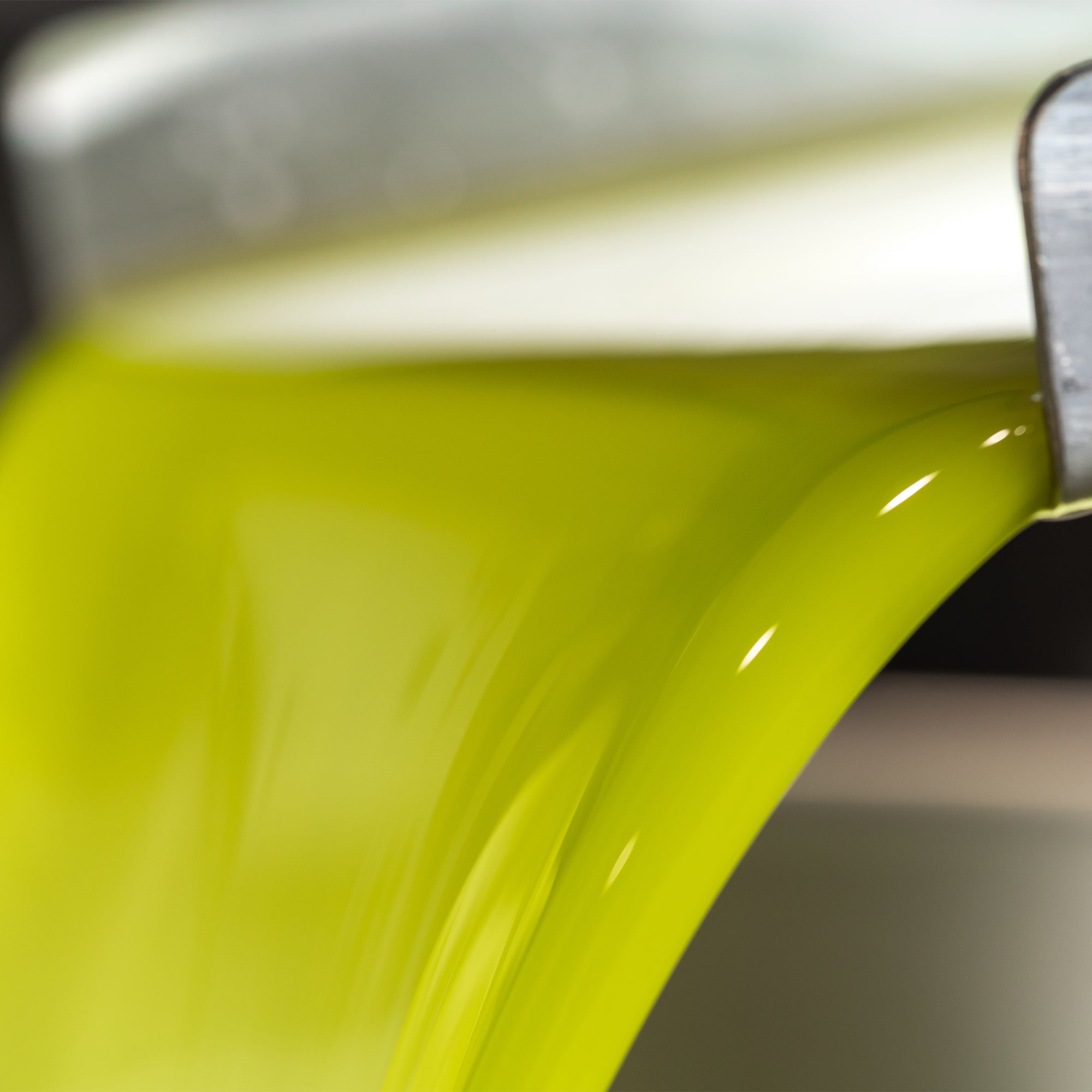 Vivid green olive oil flowing from stainless-steel milling equipment during production.