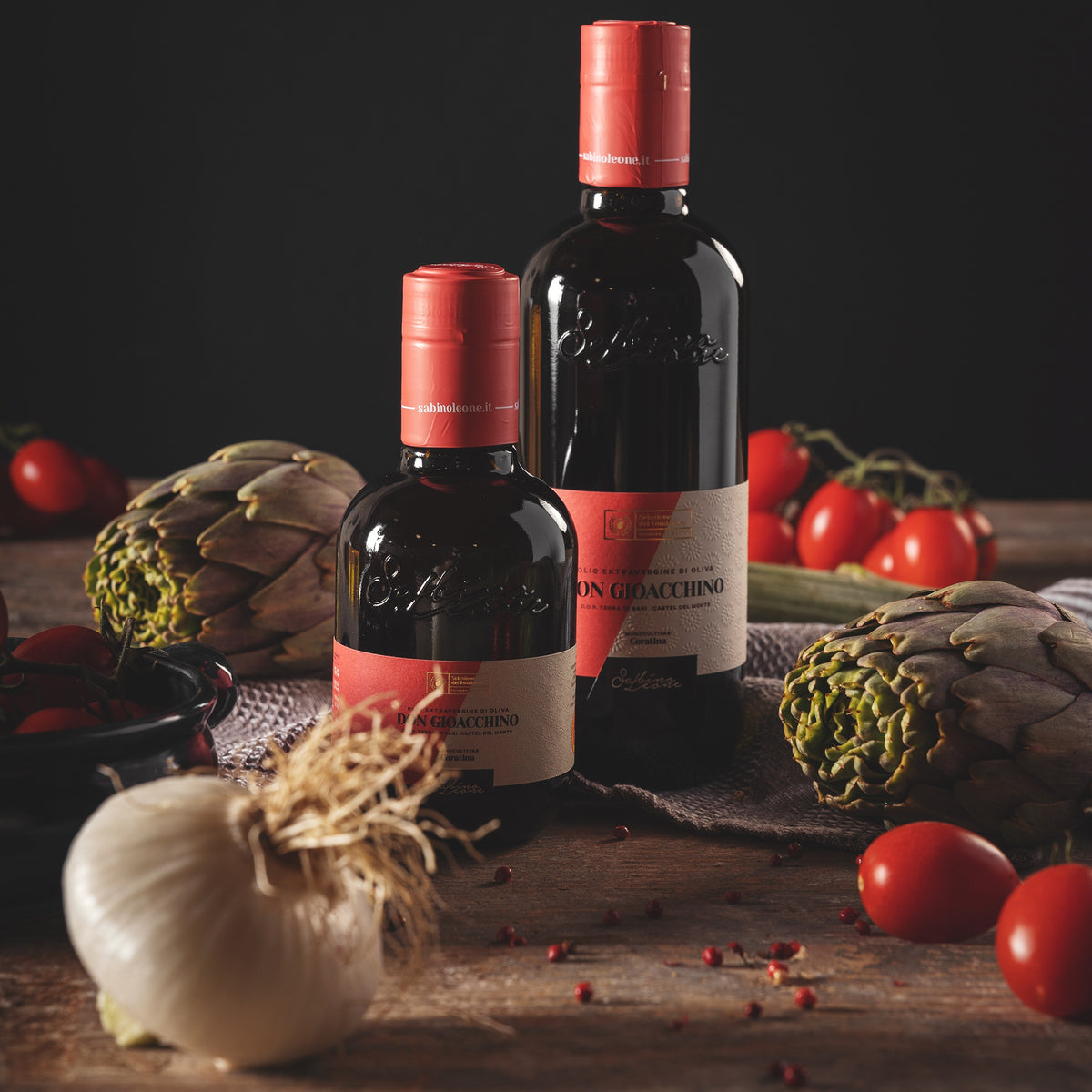 Sabino Leone Don Gioacchino olive oil bottles beside fresh artichokes, tomatoes, eggplant and garlic.