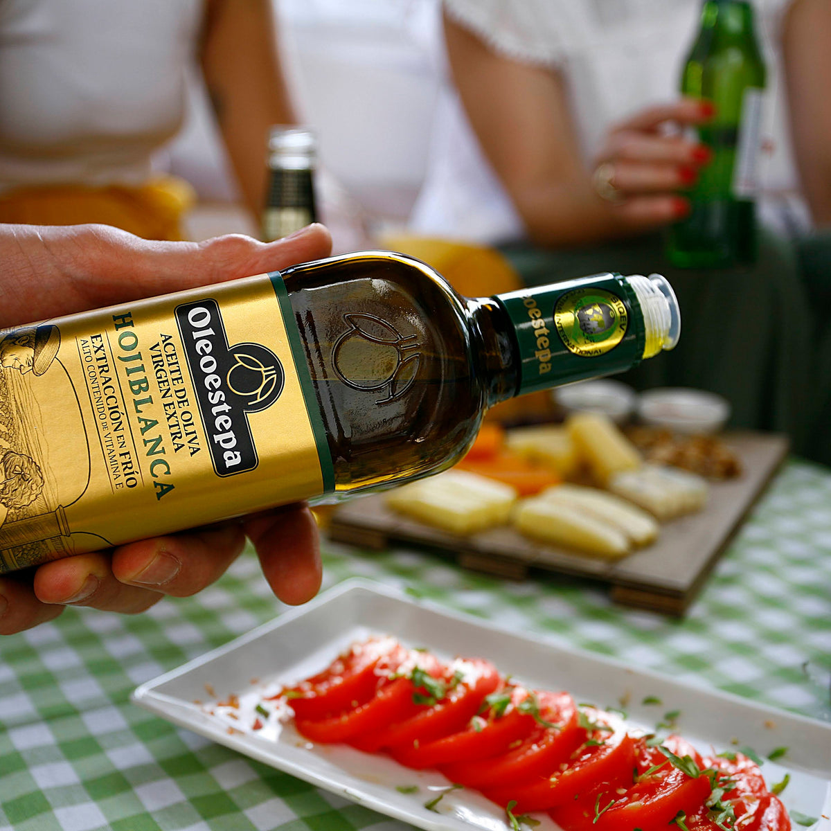 Oleoestepa Hojiblanca bottle above sliced tomatoes and cheese.