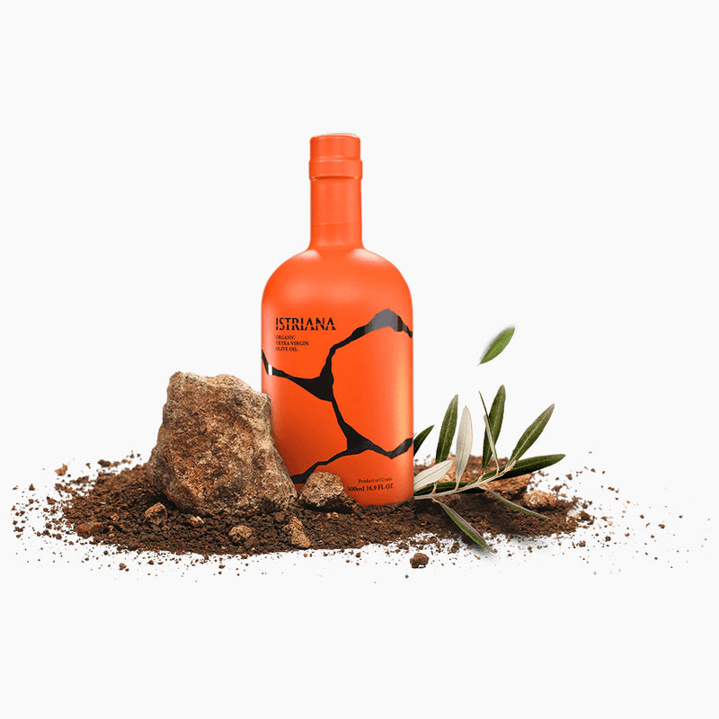 Istriana Organic 500 ml bottle among soil, natural rocks, and an olive branch.