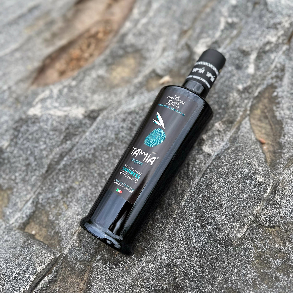 Tamia Caninese Organic 500 ml olive oil bottle on textured gray stone.