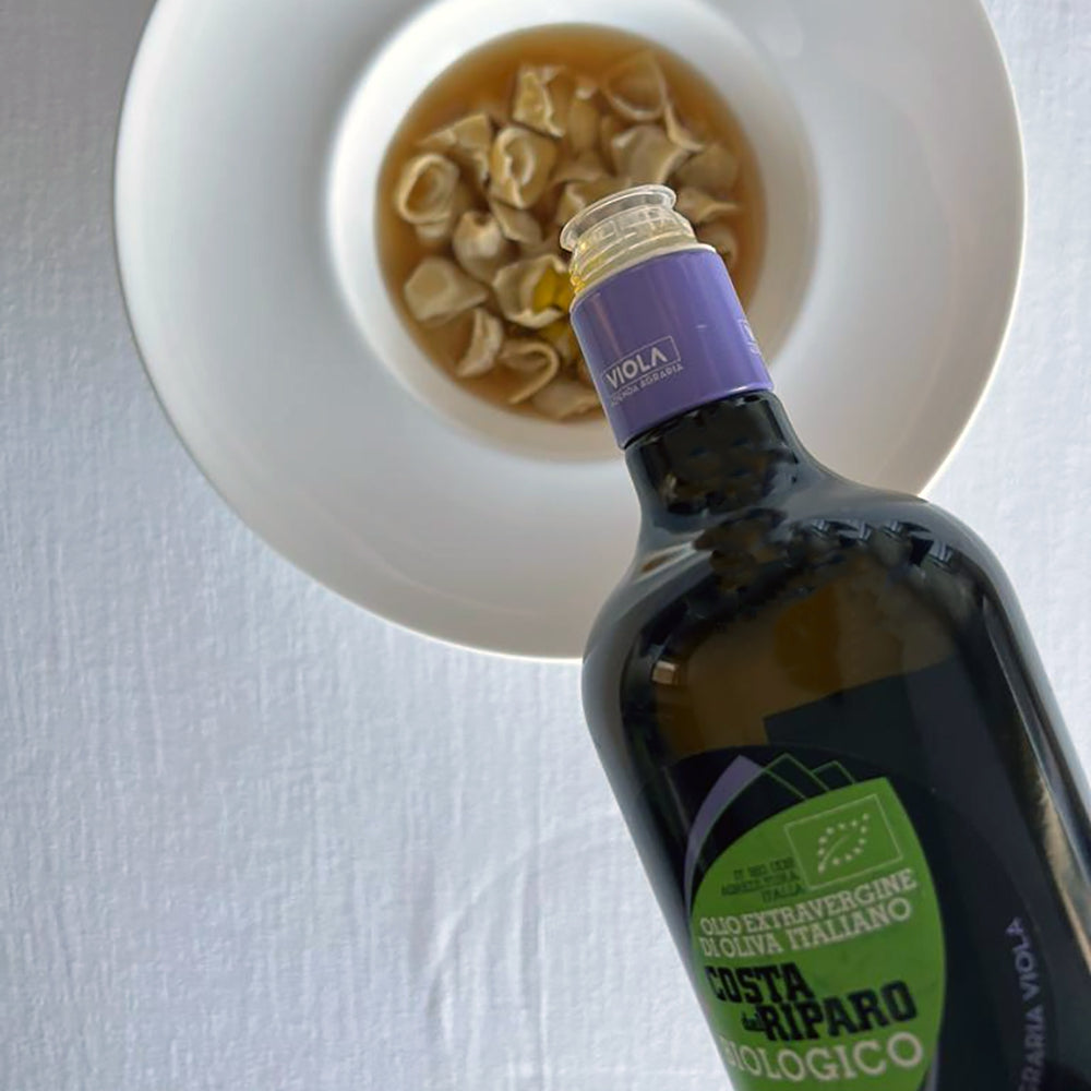 Viola Costa del Riparo Organic 500 ml olive oil bottle above a bowl of filled pasta.