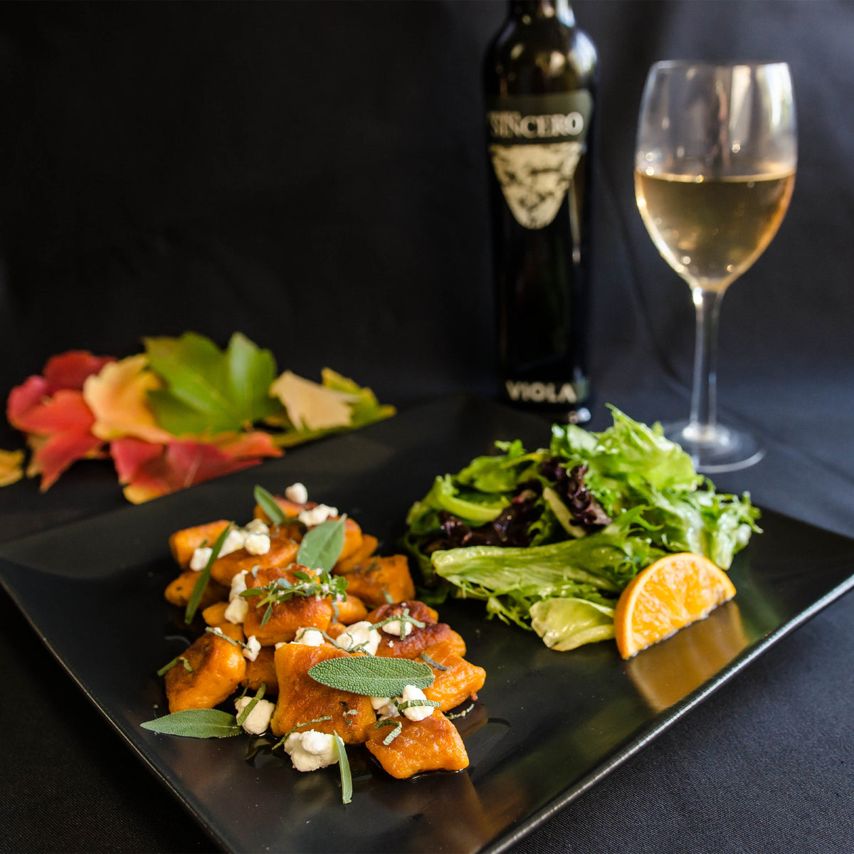 Plated gnocchi and green salad with a Viola Il Sincero bottle and glass of wine.