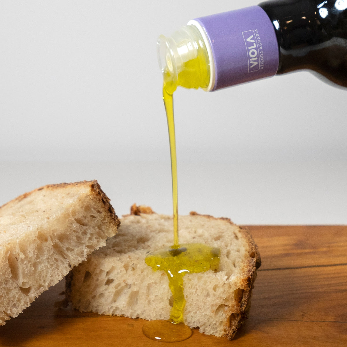 Viola extra virgin olive oil being poured over sliced bread.