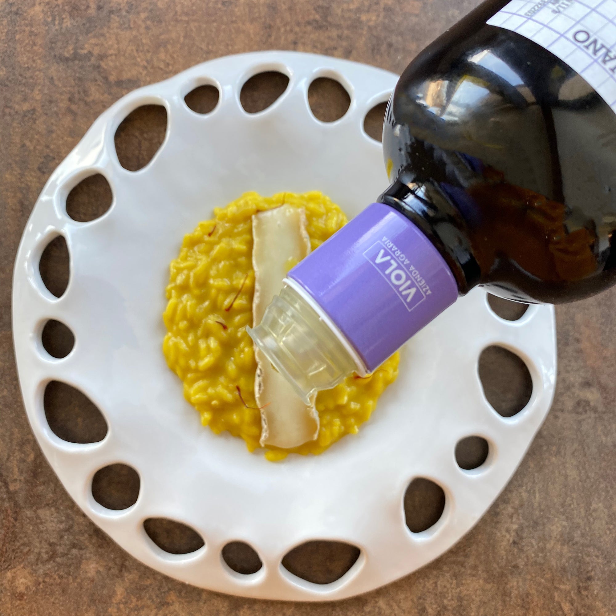 Viola olive oil being poured over risotto topped with slices of cheese.