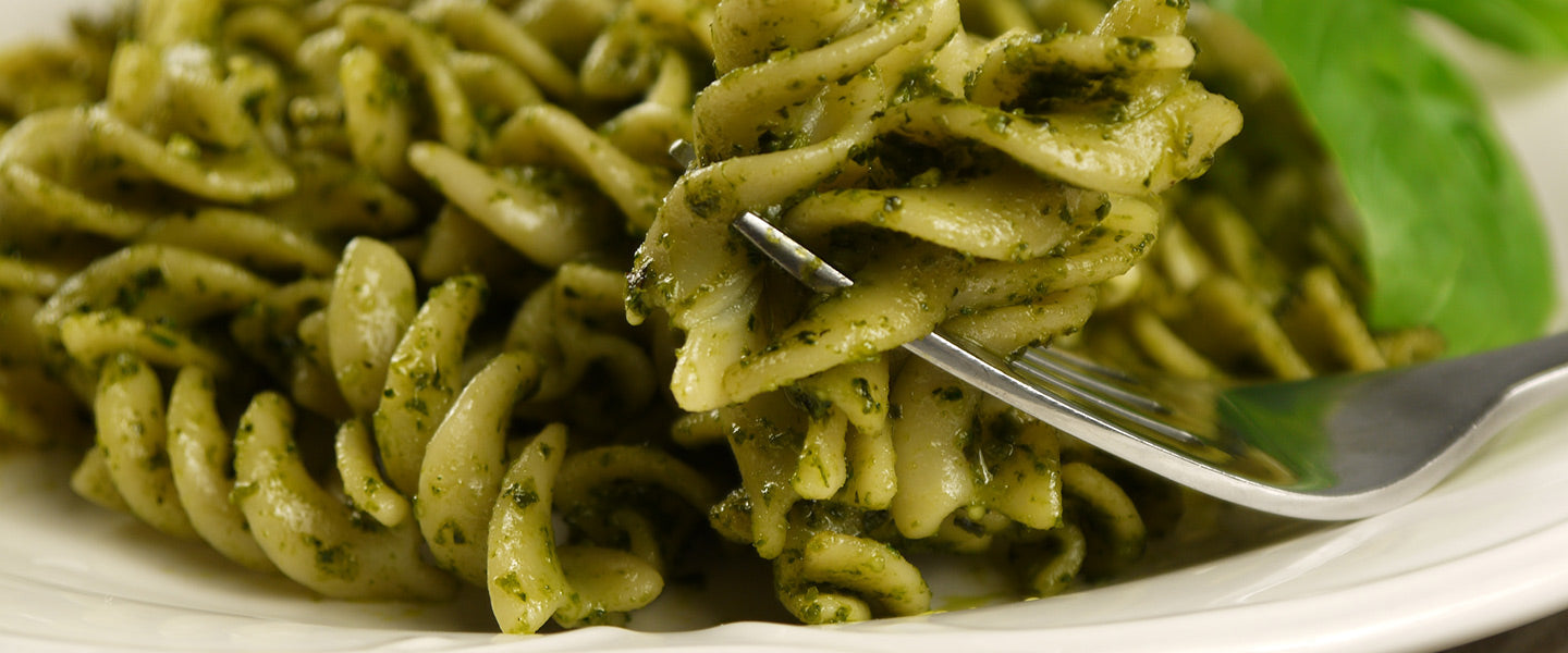Spiral pasta coated in vibrant basil pesto, with fresh basil leaves.