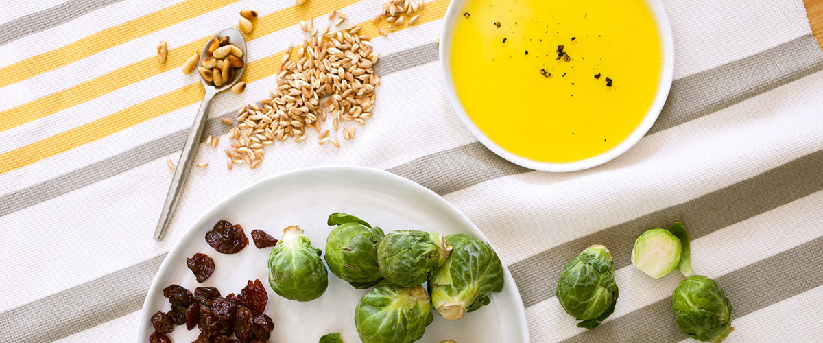 Brussels sprouts, raisins, toasted pine nuts, and grains beside a bowl of olive oil dressing.