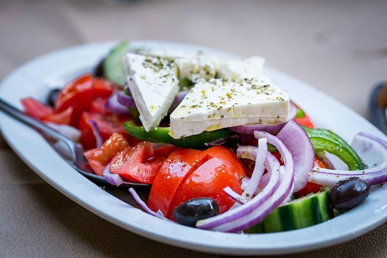 Greek salad with ripe tomatoes, cucumber, red onion, green pepper, and Greek olives, topped with thick slices of feta cheese, dried herbs, and olive oil.