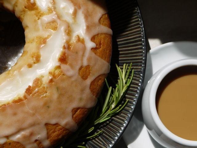Lemon rosemary cake beside a cup of coffee and garnished with a fresh rosemary sprig.