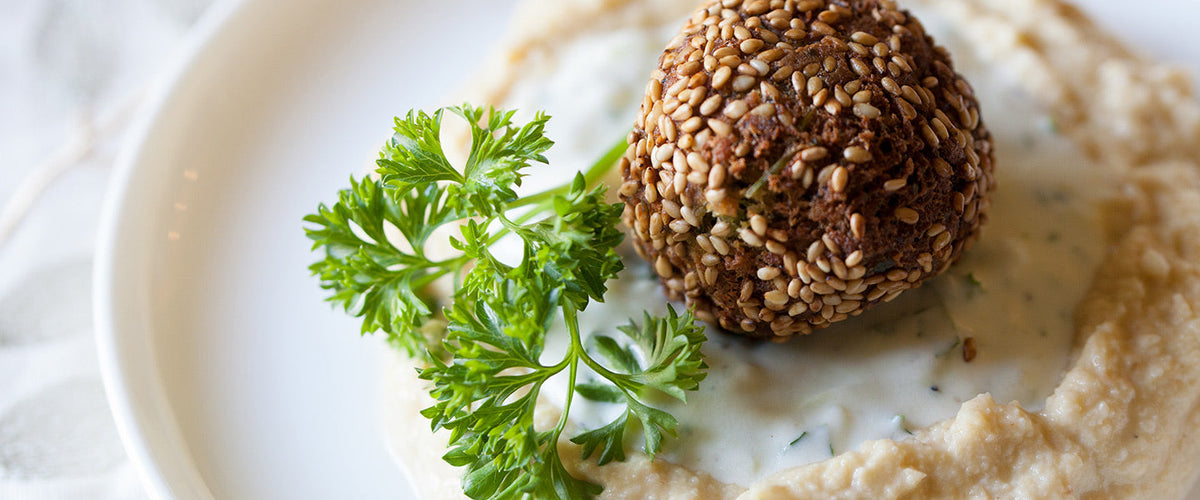 Sesame-coated falafel served with creamy hummus, herb sauce, and fresh parsley.