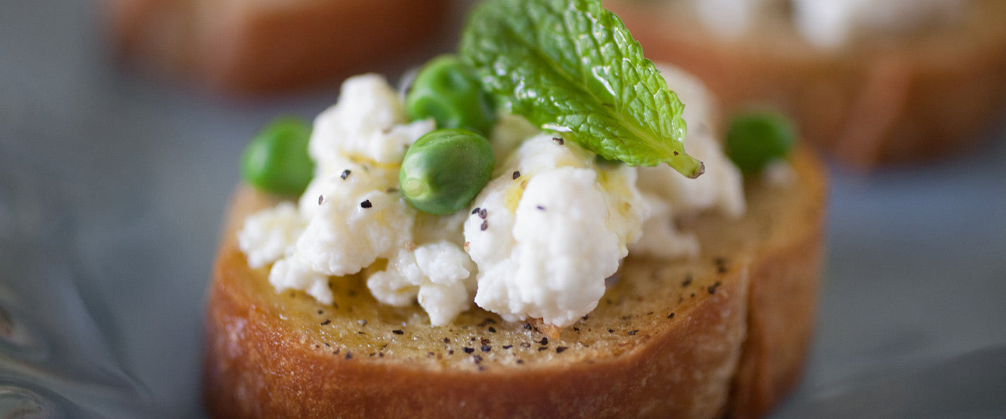 Toasted crostini topped with creamy ricotta, green peas, fresh mint, black pepper, and olive oil.