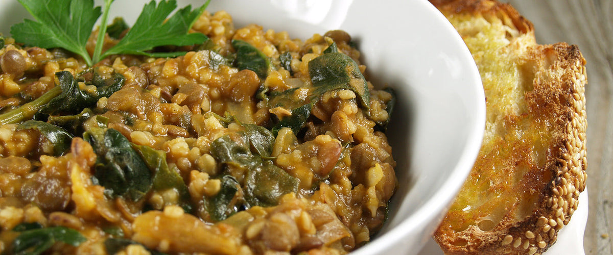 Lentil and spinach stew garnished with fresh parsley and served with olive oil.