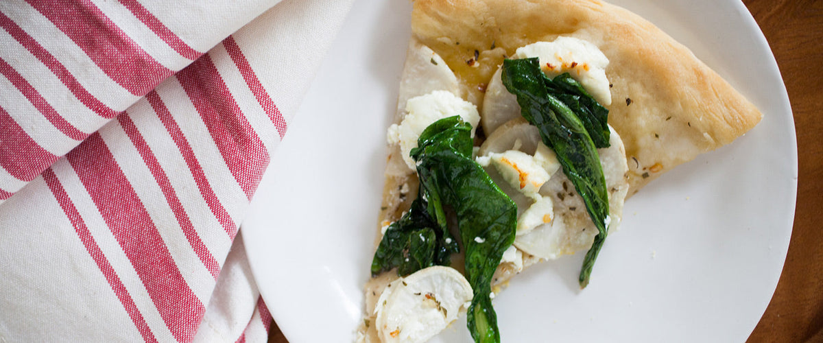 Slice of turnip pizza topped with wilted spinach, creamy ricotta, herbs, and thinly sliced roasted turnips.