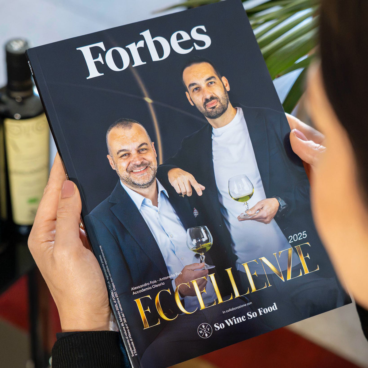 A Forbes 2025 magazine featuring Accademia Olearia representatives, with olive oil bottles behind.