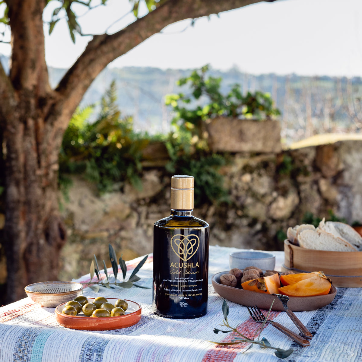 Acushla Gold Edition 500 ml bottle on an outdoor table with olives, bread, and fruit.