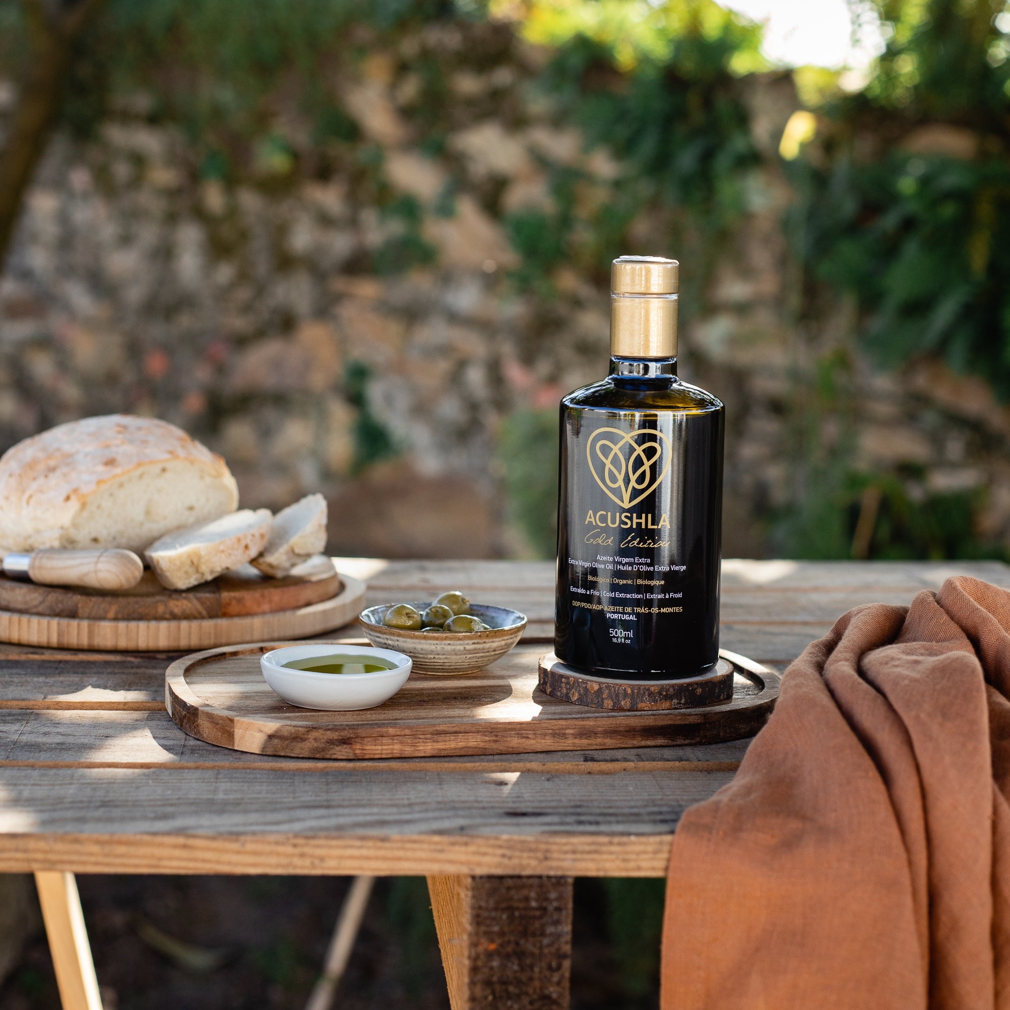 Acushla Gold Edition extra virgin olive oil on a table with bread, and green olives.