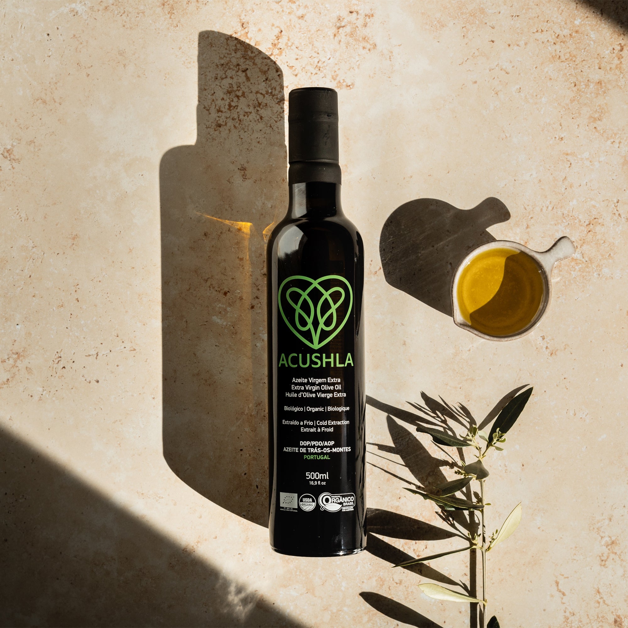 Acushla Organic DOP Trás-os-Montes 500 ml bottle beside olive oil and an olive branch.